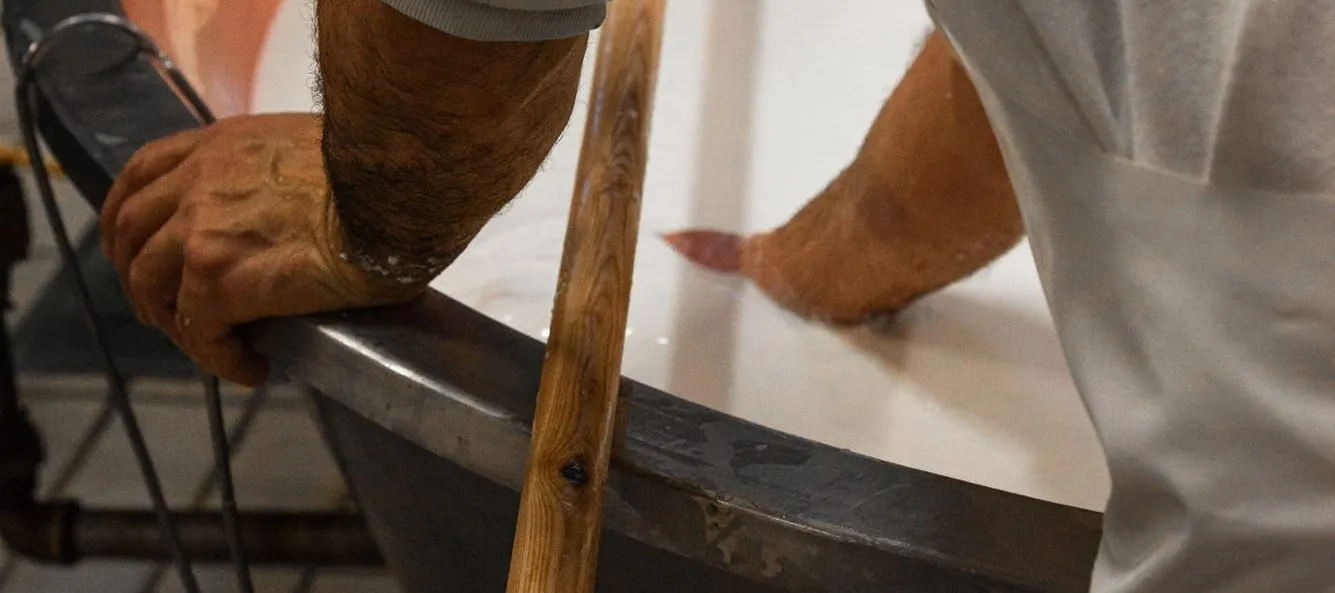 Person rührt mit einem Holzwerkzeug in einem großen Kessel